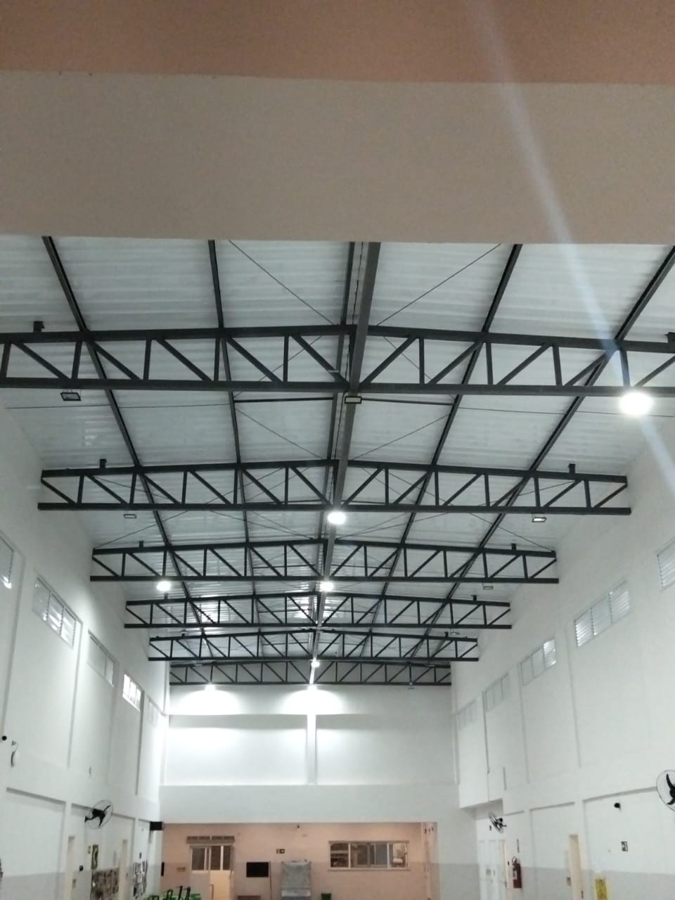 Vista ampla de luminárias e cobertura metálica em salão.